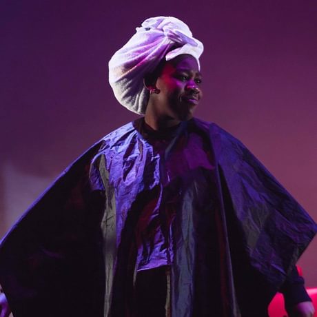 A young woman performs on stage in a hair towel and hairdressing cape