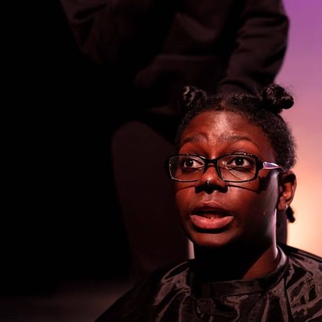 A young woman lit in purple light on stage with hair in space buns