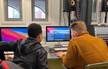 Two people work at a computer in a music studio setting