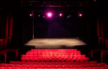 An empty auditorium with the red seats and stage lit up