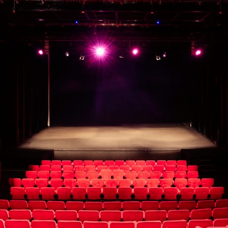 An empty auditorium with the red seats and stage lit up
