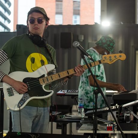 A young man plays guitar, wearing sunglasses and looking effortlessly cool in a skate park
