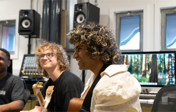 three laughing young men of different ethnicities play guitars