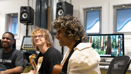 three laughing young men of different ethnicities play guitars