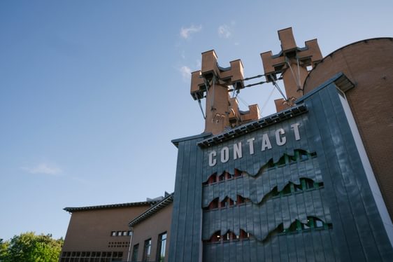 The contact exterior shot from a low angle, showing the building's turrets and grey metal facade against a blue sky