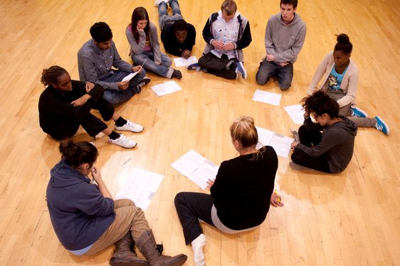 A group of young people sit on the floor in a circle during a workshop