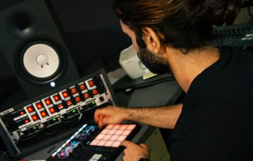 A young man with dark hair and a beard experiments with equipment in a music studio