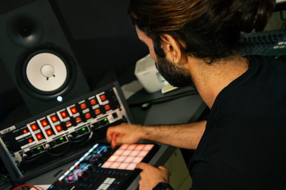 A young man with dark hair and a beard experiments with equipment in a music studio