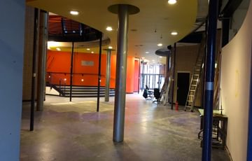 An empty ground floor foyer ready for reconstruction. There are a few ladders leaning against the walls on the right.
