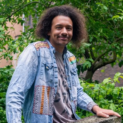 A young man sits in a denim shirt surrounded by green leaves