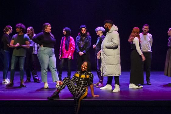 image shows a group of people standing talking on the stage. keisha thompson is sitting at the front of the stage.