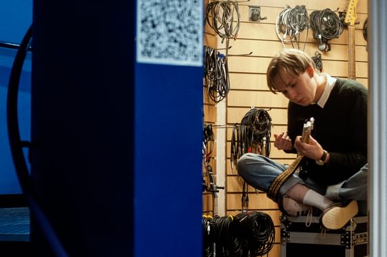 A young man plays guitar surrounded by music equipment