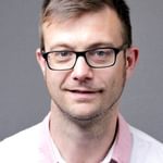 Headshot of Jerome, He is wearing a white shirt with pink collars. His hair is short and brown and he's wearing glasses with a black frame.