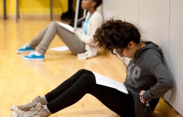 A young person sits in a rehearsal room reading a script on their knees