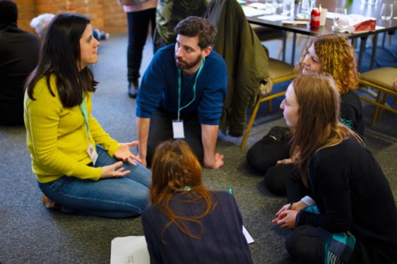A group of people sat on the floor talking and writing notes.