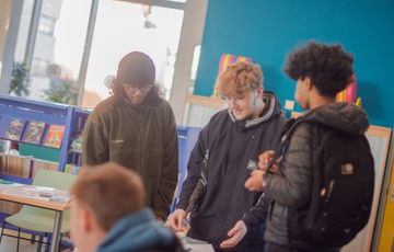 Three young people wait in a blue walled room