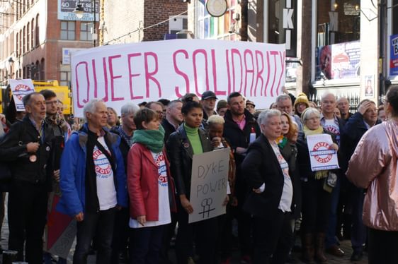 A group of people protest on Canal St in Manchester holding a large banner