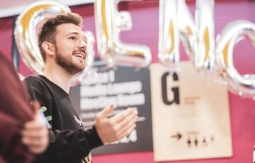 A young man stands under balloons reading AGENCY whilst addressing a room of people