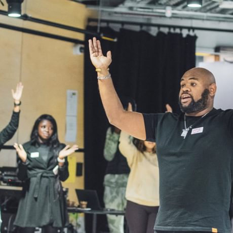 A man stands waving his arms in a room of young people