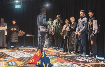 A group of young people play a giant board game in a studio room