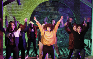 A group of people performing on stage and they all have their arms up.