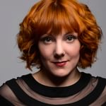 A white woman with short red curly hair and a black top